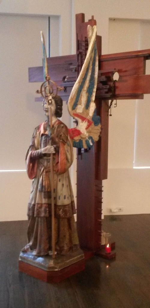 "Resurreccion”/”Resurrection” by Rafael Queneditt. 2013. From the exhibition: Drapetomania: Grupo Antillano and the Art of Afro-Cuba. (Photo: Kris Juncker.) Queneditt's sculptural installation centers upon a figure of the archangel Raphael. Nails driven into the side of the crucifix reference practices in Regla de Ocha and Palo (where nails may be added to certain objects to appeal to specific divinities).